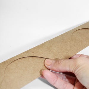 Può includere: Un modello di carta marrone con due ritagli curvi. Il modello è tenuto da una mano.