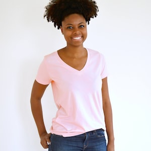 Puede incluir: Una mujer con una camiseta rosa claro de cuello en V y pantalones vaqueros azules.