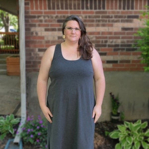 Puede incluir: Una mujer con un vestido maxi gris carbón con cuello redondo y tirantes finos. Lleva sandalias marrones y gafas.