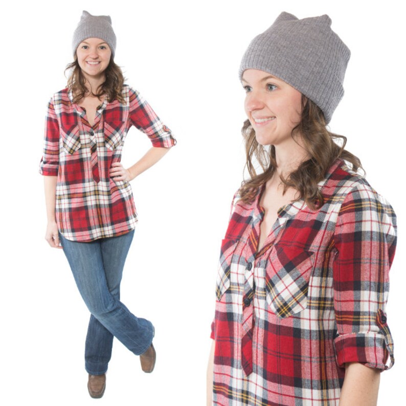 May include: Two women wearing red and black plaid shirts with grey beanies. The women are standing in front of a white background.