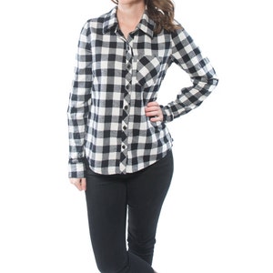 May include: A woman wearing a black and white plaid flannel shirt with long sleeves and a button-up front. She is wearing black jeans and brown boots.