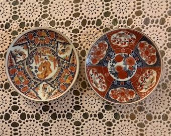 May include: Two decorative ceramic plates with intricate floral and geometric designs in shades of red, blue, and gold. The plates feature traditional Japanese motifs.