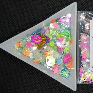 Pode incluir: Um saco de plástico transparente cheio de glitter holográfico iridescente, com um cartão branco no interior que diz "Star Stuff LnA" e "Take me to your dealer".