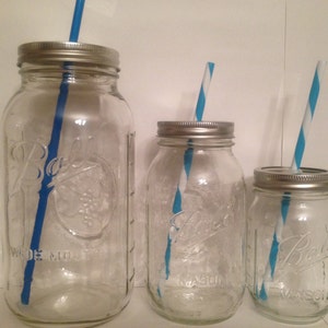 May include: Three clear glass mason jars of varying sizes with silver lids and blue and white striped straws. The jars have the "Ball" logo and "Wide Mouth" text. The jars are empty.