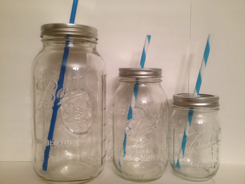 May include: Three clear glass mason jars of varying sizes with silver lids and blue and white striped straws. The jars have the "Ball" logo and "Wide Mouth" text. The jars are empty.