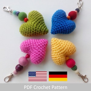 May include: Four crocheted heart-shaped keychains in green, blue, pink, and yellow with colorful bead accents.  The keychains are displayed on a white surface with the text "PDF Crochet Pattern" and flags of the United States and Germany.