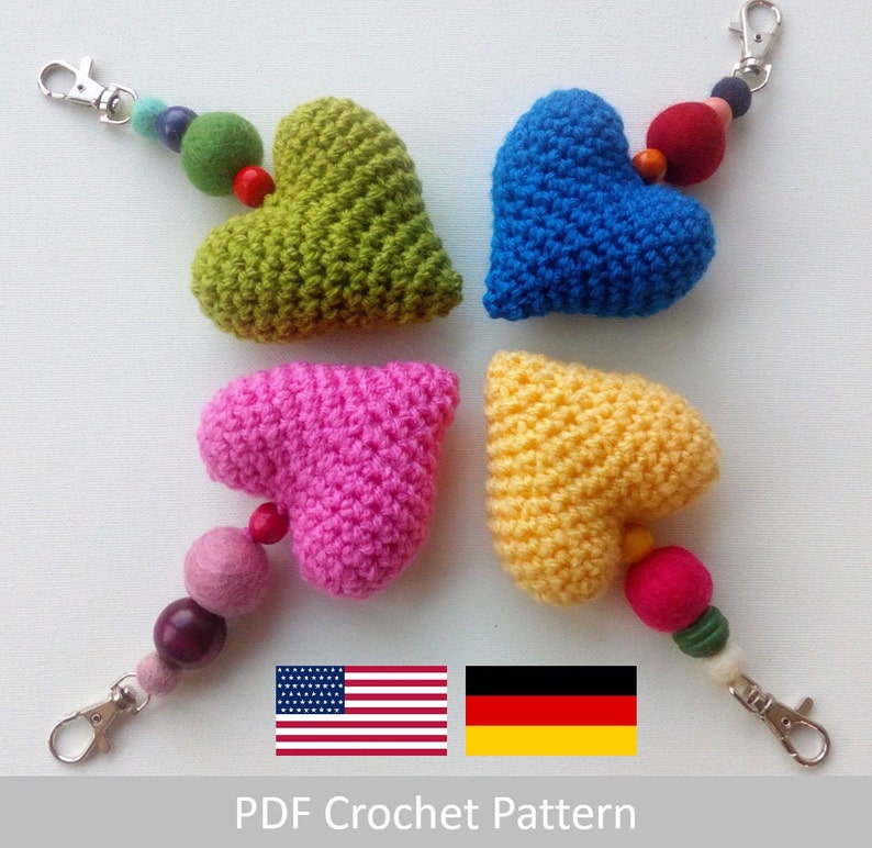 May include: Four crocheted heart-shaped keychains in green, blue, pink, and yellow with colorful bead accents.  The keychains are displayed on a white surface with the text "PDF Crochet Pattern" and flags of the United States and Germany.