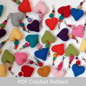 May include: A collection of crocheted heart keychains in various colors, including red, pink, blue, green, yellow, and purple. Each keychain features a heart-shaped charm with a beaded chain attached to a metal ring.