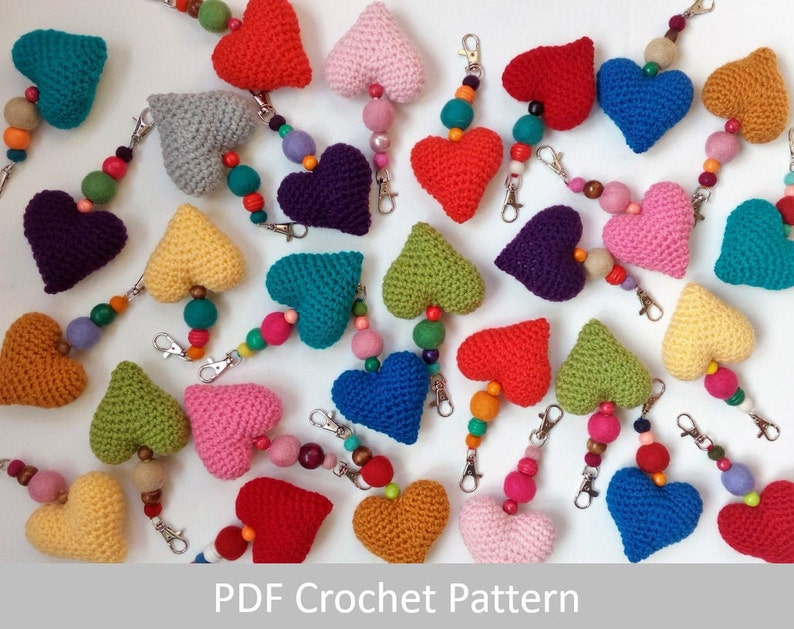 May include: A collection of crocheted heart keychains in various colors, including red, pink, blue, green, yellow, and purple. Each keychain features a heart-shaped charm with a beaded chain attached to a metal ring.