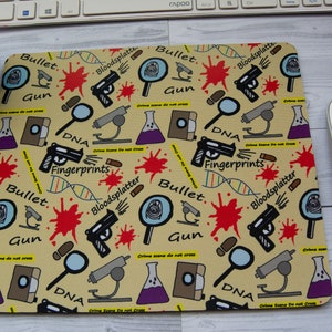May include: A yellow mouse mat with a repeating pattern of crime scene related illustrations. The illustrations include a magnifying glass, a gun, a vial of purple liquid, a microscope, a bullet, a strand of DNA, and the words "Bloodsplatter", "Bullet", "Gun", "DNA", "Fingerprints", and "Crime Scene Do Not Cross".