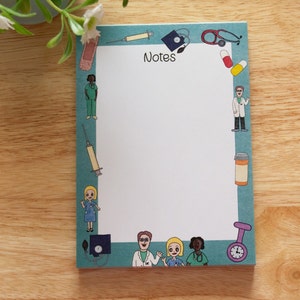 May include: A blue notepad with a white border and the word "Notes" printed in black. The border is decorated with medical-themed illustrations, including a stethoscope, a syringe, a pill bottle, a bandage, and cartoon doctors and nurses.