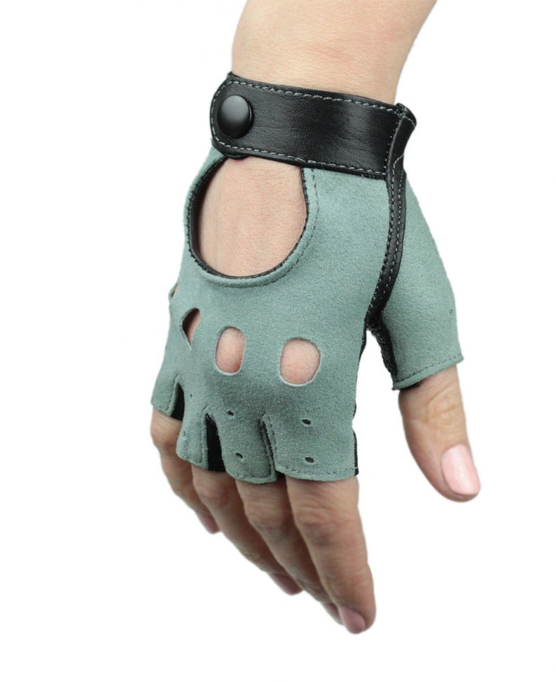 May include: A pair of fingerless driving gloves with a green suede palm and black leather wrist strap. The gloves have a button closure and finger holes.