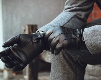 May include: A pair of black leather gloves with a button fastening on the wrist. The gloves are made from soft, supple leather and have a classic design.