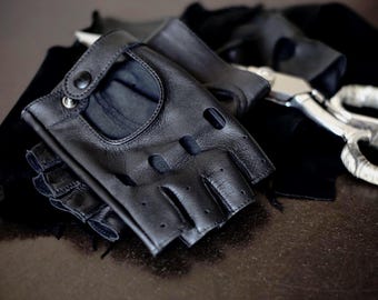 Puede incluir: Un par de guantes sin dedos de cuero negro con un diseño de agujero para los dedos. Los guantes están hechos de cuero suave y flexible y tienen un aspecto elegante y moderno.