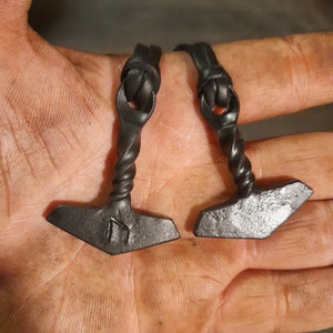 May include: Two black leather bracelets with a twisted metal hammer charm. Each charm has a rune symbol engraved on it.