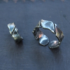 May include: Two silver-toned metal rings with an abstract, textured design. The rings have an open design, with irregular, overlapping shapes. The metal has a slightly tarnished appearance, giving it a vintage look.