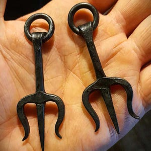 K&ouml;nnte beinhalten: Zwei schwarze Metalltridents mit einem Ring an der Oberseite jedes Griffs.