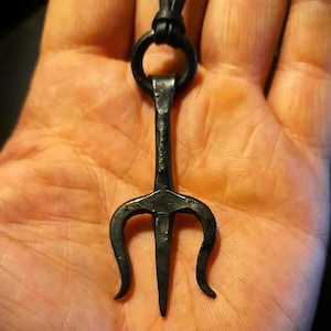 以下が含まれることがあります： 黒い革ひもに黒い金属製の三叉のペンダント。ペンダントの長さは約5cmで、シンプルでミニマルなデザインです。