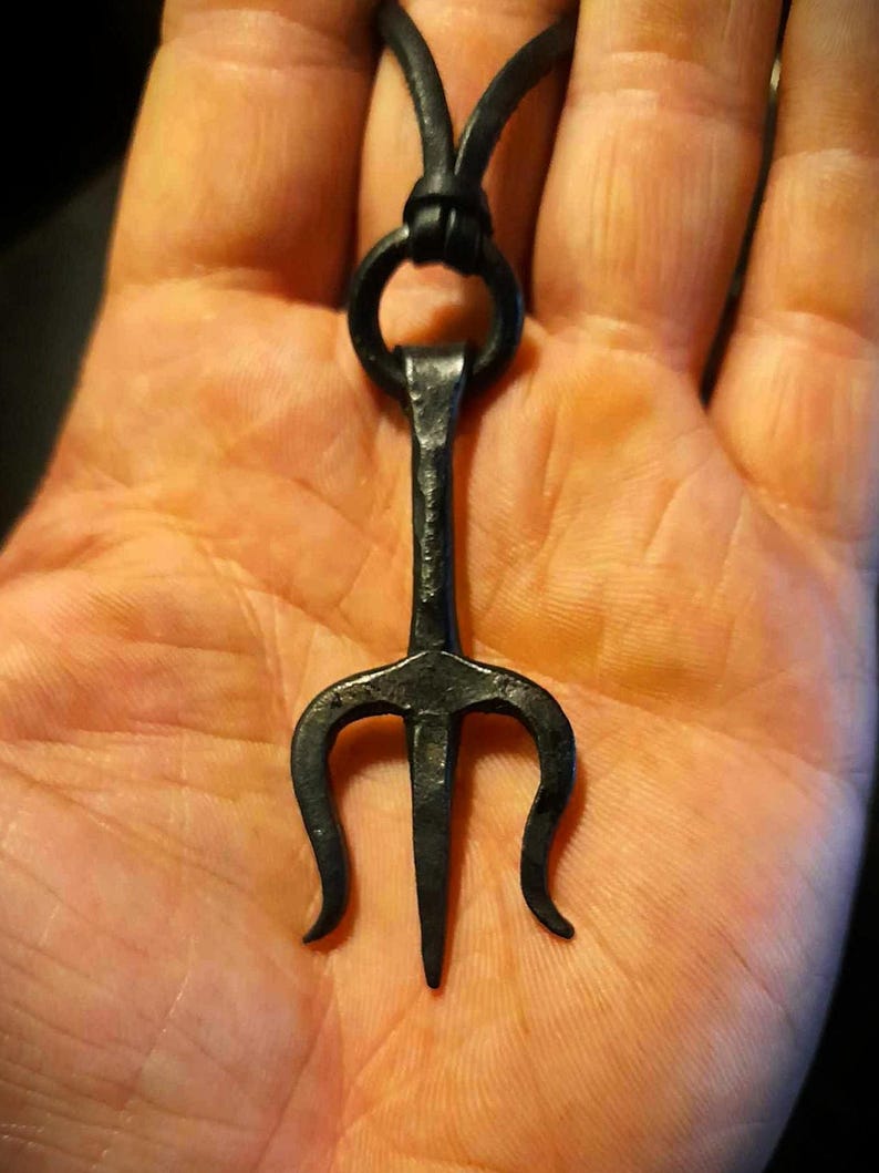 K&ouml;nnte beinhalten: Ein schwarzer Metall-Dreizack-Anh&auml;nger an einem schwarzen Lederband. Der Anh&auml;nger ist etwa 5 cm lang und hat ein schlichtes, minimalistisches Design.