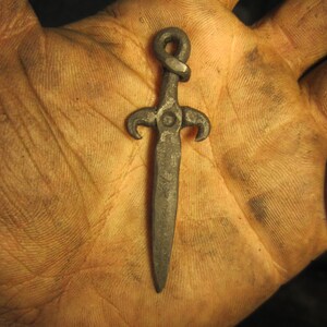 May include: A small, silver-colored, sword-shaped pendant with a twisted knot at the top.