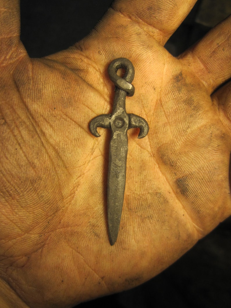 May include: A small, silver-colored, sword-shaped pendant with a twisted knot at the top.