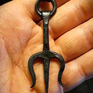 K&ouml;nnte beinhalten: Schwarzer Metall-Trident-Anh&auml;nger mit einem Lederband. Der Dreizack hat drei Zacken und einen Ring oben.