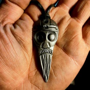 May include: A silver pendant necklace with a detailed skull design. The pendant is shaped like a teardrop and has a textured surface.