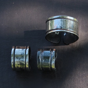 May include: Three silver metal napkin rings. The rings are all different sizes and have a hammered finish.