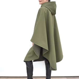 May include: Olive green hooded cape with a flowing design. The cape features a hood and a loose fit. The garment is made of a smooth, solid-coloured fabric, suitable for outerwear.