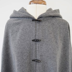 May include: A gray hooded cape with black toggle closures. The cape is made of a soft, fuzzy fabric.