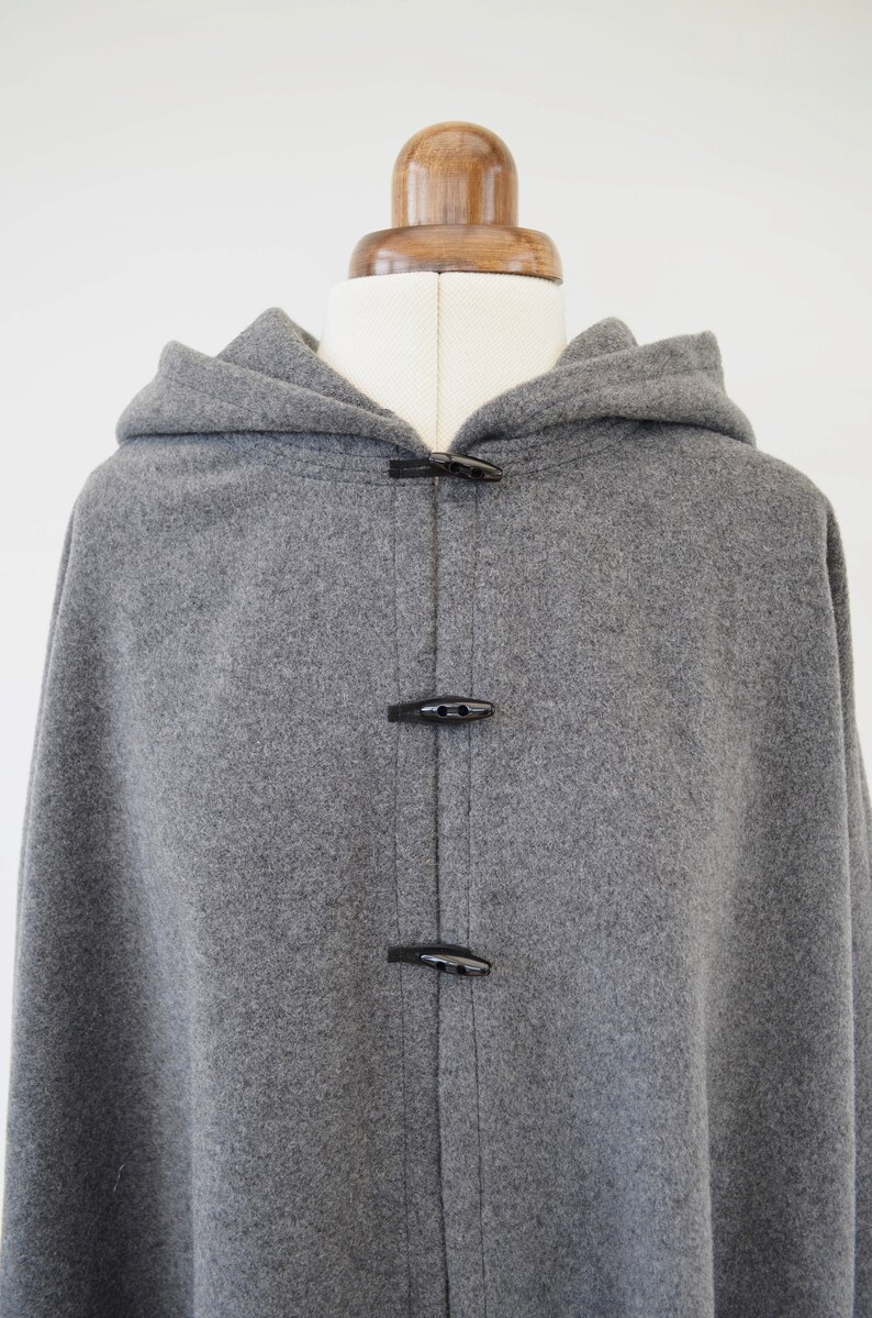 May include: A gray hooded cape with black toggle closures. The cape is made of a soft, fuzzy fabric.