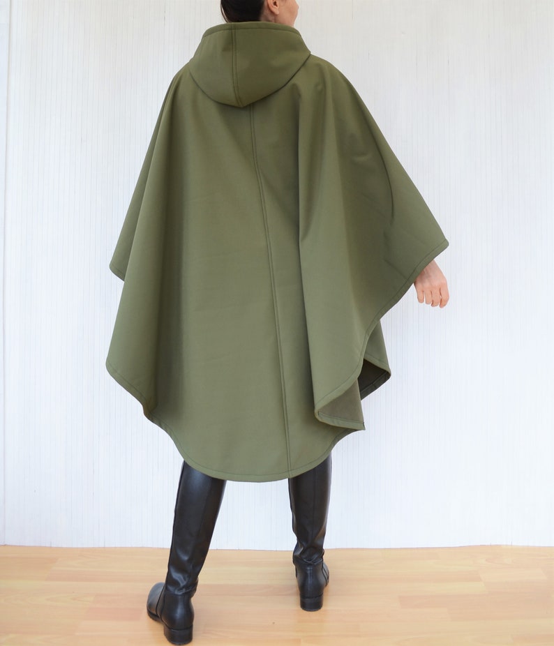 May include: An olive green hooded cape with a flowing design. The cape has a simple silhouette and is made of a smooth, solid-coloured fabric. The model is wearing black boots.