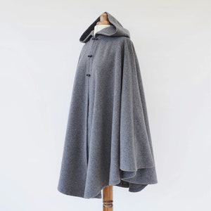 May include: A gray hooded cape with a long, flowing design. The cape is made of a soft, warm fabric and has a simple, elegant style.