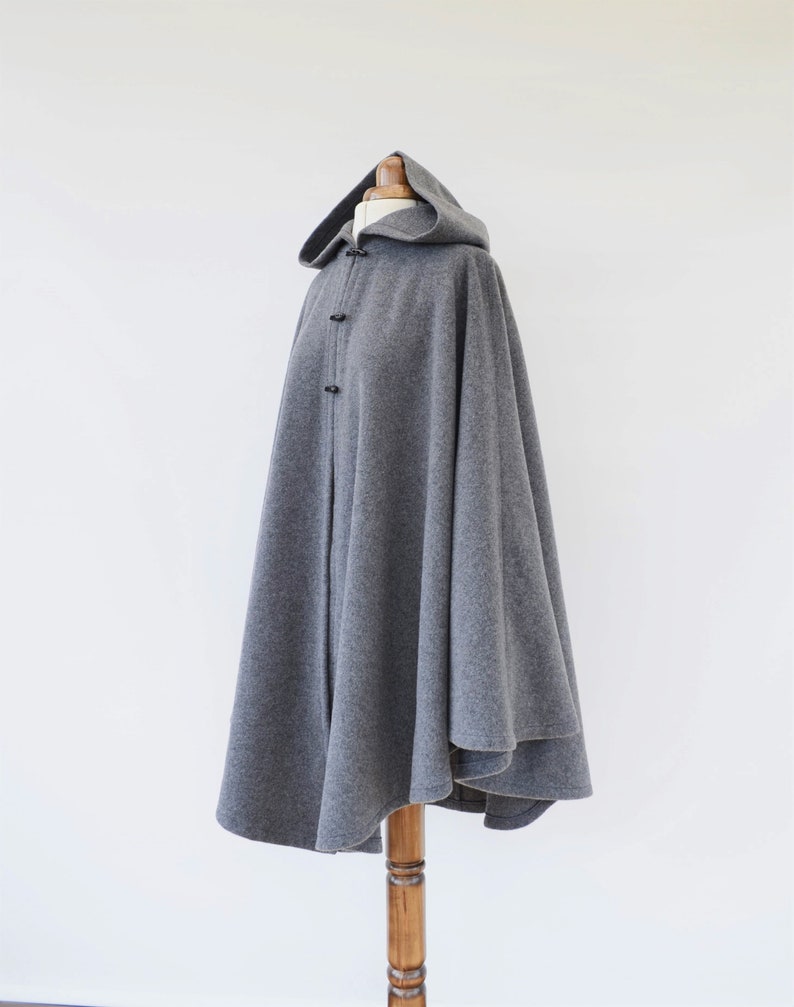 May include: A gray hooded cape with a long, flowing design. The cape is made of a soft, warm fabric and has a simple, elegant style.