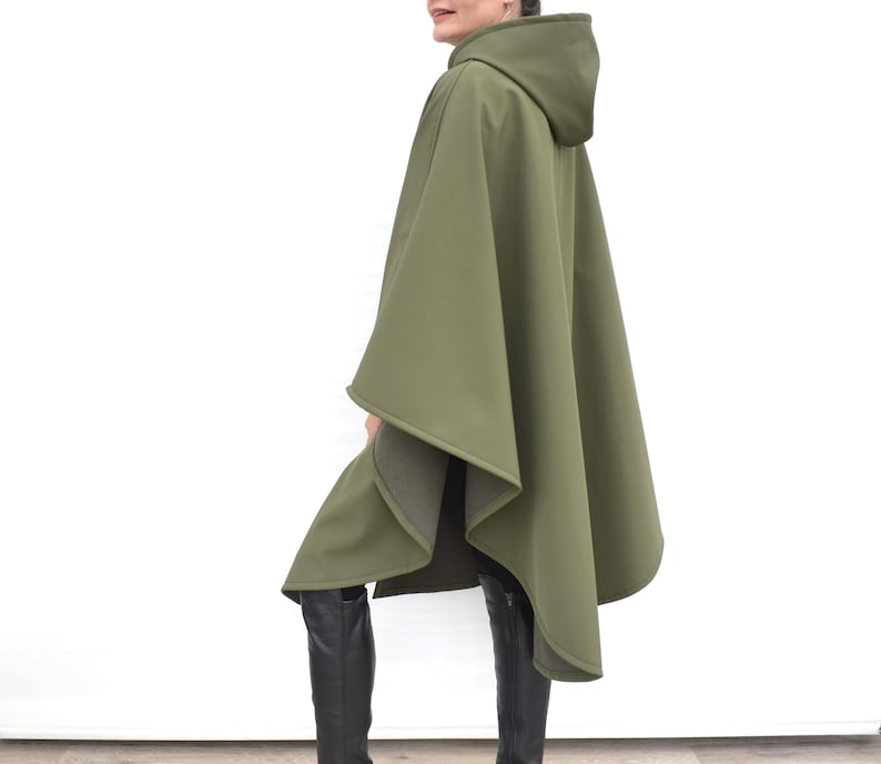 May include: Olive green hooded cape with a flowing design. The cape features a hood and a loose fit. The garment is made of a smooth, solid-coloured fabric, suitable for outerwear.