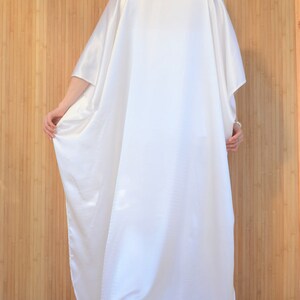 May include: A white satin kaftan with long sleeves and a loose fit. The kaftan is flowing and drapes beautifully.