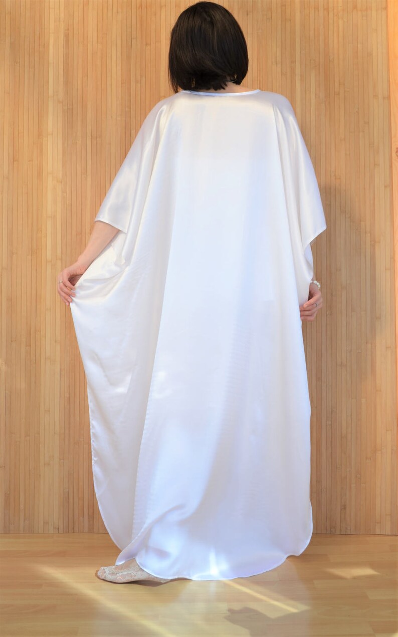 May include: A white satin kaftan with long sleeves and a loose fit. The kaftan is flowing and drapes beautifully.