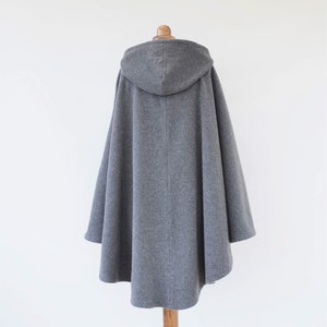 May include: A gray hooded cape with a long, flowing design. The cape is made of a soft, warm fabric and has a relaxed fit.