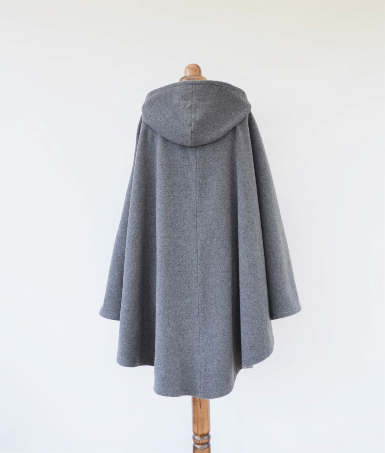 May include: A gray hooded cape with a long, flowing design. The cape is made of a soft, warm fabric and has a relaxed fit.