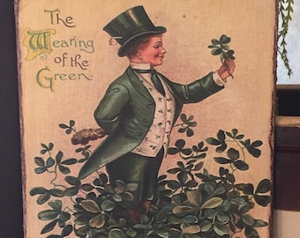 May include: A vintage postcard featuring a cartoon illustration of a man wearing a green suit, a top hat, and holding a four-leaf clover. The text "The Wearing of the Green" is at the top of the postcard.