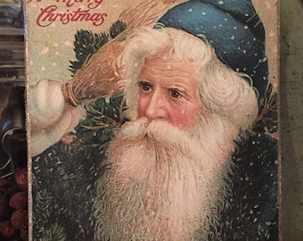 May include: Vintage Christmas card featuring a portrait of Santa Claus with a long white beard and a blue hat. The card has the text "A Merry Christmas" in red script. The image is surrounded by evergreen branches.