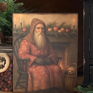 May include: A framed print depicts an elderly man with a long white beard, wearing a red robe and sitting in a wooden chair. The background shows a fireplace, candles, and a small teddy bear in a basket, evoking a cozy, vintage Christmas theme.