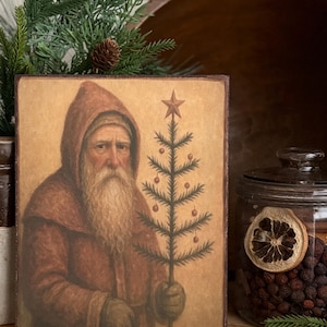 May include: A vintage-style square print depicts a robed figure with a long white beard holding a small Christmas tree. The figure wears a hooded robe in shades of brown and red. The tree is adorned with small red ornaments and a star.