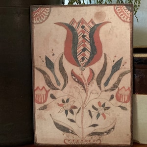 May include: A vintage-style tile with a hand-painted floral design. The tile features a red, blue, and black tulip with two smaller flowers below. The tile has a cream-colored background and a brown border.