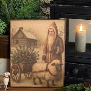 May include: A rectangular wooden sign with a vintage illustration of Santa Claus, a sheep, and a cart filled with greenery. The artwork has a rustic, aged appearance, with a log cabin in the background. The color palette is muted, with browns, greens, and creams.