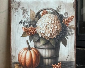 May include: A rectangular wooden sign with a rustic, distressed finish. The artwork depicts a fall scene with a pumpkin, a wooden bucket overflowing with flowers, and berries. The color palette includes shades of orange, brown, and cream.