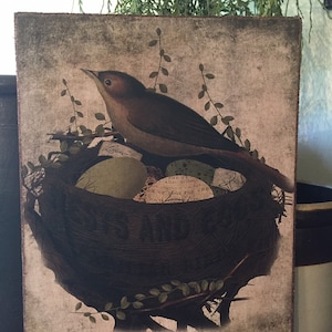 May include: A vintage-style print of a bird sitting on a nest of eggs. The print has a distressed, aged look and is framed in a rustic wood frame.