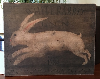 May include: A vintage-style sign with a white rabbit running across a dark brown background. The sign reads "White Rabbit Inn Est. 1784".