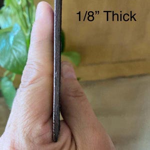 May include: A close-up of a brown leather strip held in a hand. The leather is 1/8 inch thick.