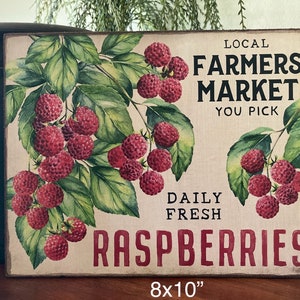 May include: A rectangular wooden sign with a vintage design. It features a watercolor illustration of raspberries and green leaves. The sign reads "Local Farmers Market, You Pick, Daily Fresh Raspberries." The sign measures 8x10 inches.